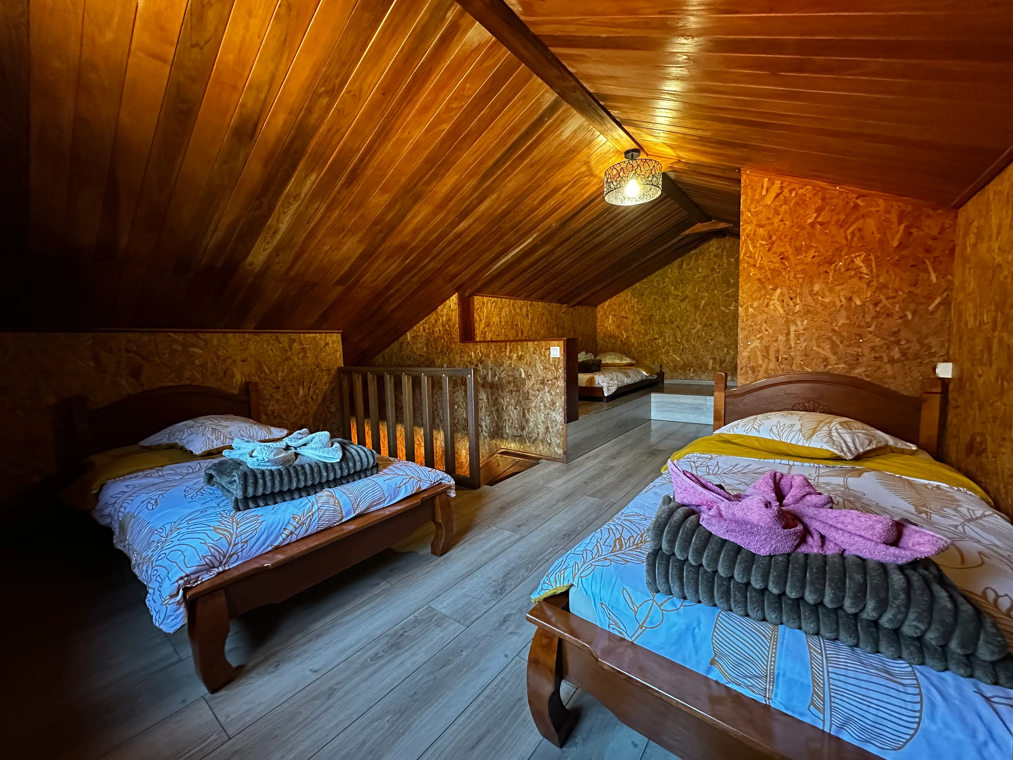 Dortoir 4 places sous les toits : lits simples en bois, serviettes pliées, charpente apparente