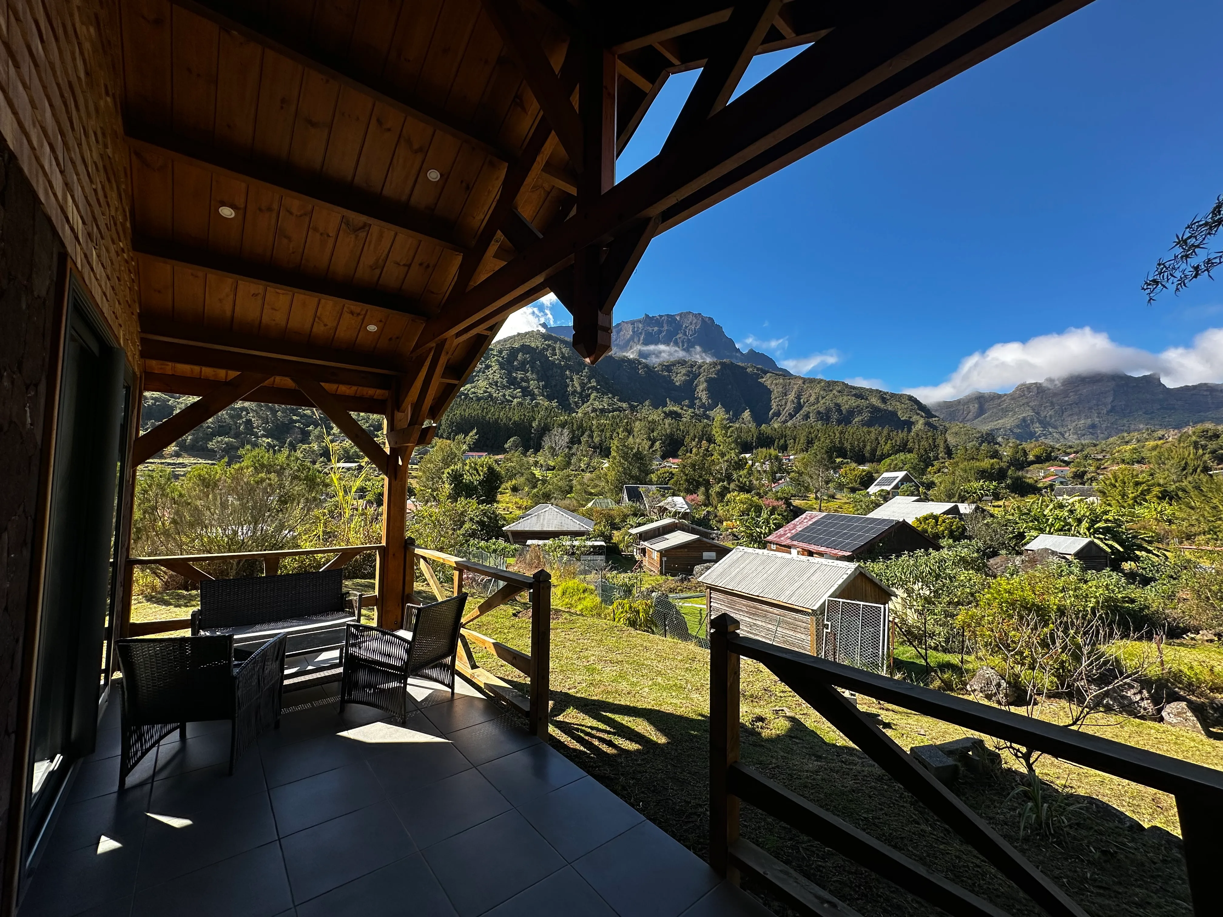 La vue depuis la terrasse couverte du gîte : les toits de La Nouvelle, la forêt et les remparts du cirque sous un ciel bleu